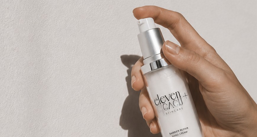 A hand holds a bottle of  hand serum above another open hand showing a small amount of white cream, set against a textured white wall with dramatic diagonal shadows.